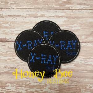 May include: Four black felt circles with white stitching around the edges. Each circle has the text "X-RAY" embroidered in blue thread.