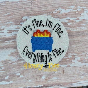 May include: A white circle with glitter, featuring a black and white embroidered design of a dumpster on fire with the text "It's fine, I'm fine, Everything is fine."  The text "Honey Bee Designs" is also embroidered in black and white.