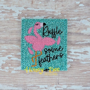May include: Embroidered patch with a pink flamingo and the text "Ruffle some feathers". The background is a turquoise glitter fabric. The patch is from Honey Bee Designs.