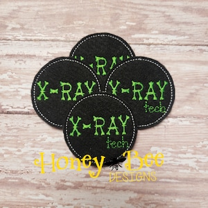 May include: Four black felt circles with white stitching around the edges. Each circle has the text "X-RAY" in green embroidery. The text "teeth" is embroidered below the text "X-RAY" on two of the circles. The text "Honey Bee Designs" is printed below the circles.