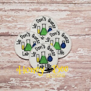 May include: Five white round embroidered patches with the text "We Don't Guess" and a beaker, test tube, and flask. The text "Lab Life" is on two of the patches.
