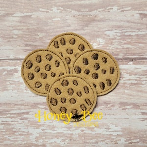 May include: Four brown felt coasters with a chocolate chip cookie design. The coasters are round and have a brown felt backing. The design is embroidered in black thread.