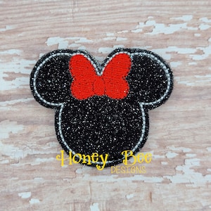May include: Black and white glitter iron-on applique with a red bow. The applique is shaped like a cartoon mouse head with large ears.