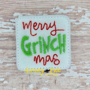 May include: White felt square with red and green embroidered text that reads "merry Grinch mas".