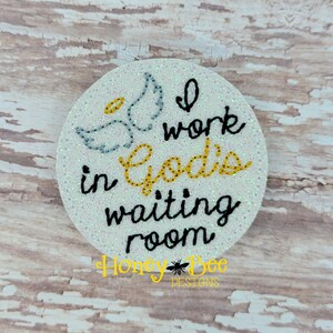 May include: A white round ornament with glitter, featuring a gray angel wing design and the text "I work in God's waiting room".