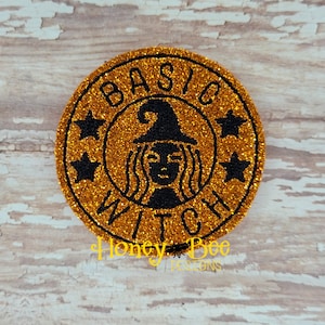 May include: A gold glitter circle with the text "BASIC WITCH" in black lettering. A black silhouette of a witch with a pointed hat is in the center of the circle.