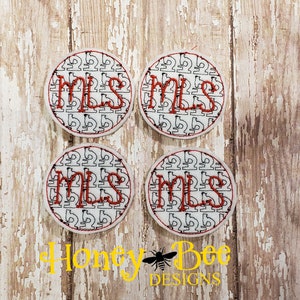 May include: Four white round fabric patches with a black and white pattern. The word "MLS" is embroidered in red on each patch.