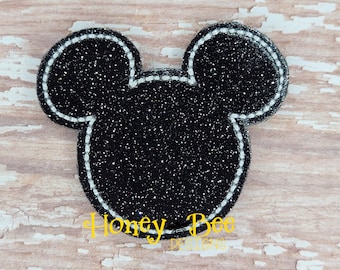 May include: Black glitter iron-on applique in the shape of a Mickey Mouse head with a white outline.