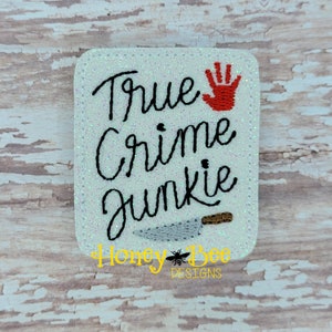 May include: White square patch with glitter, embroidered with the text "True Crime Junkie" in black, a red handprint, and a black knife with a brown handle. The text "Honey Bee Designs" is embroidered in black at the bottom.