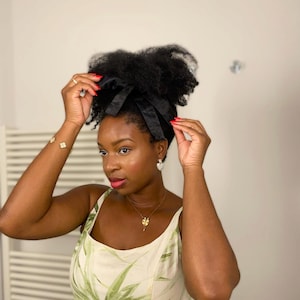 Può includere: Un nastro di raso nero legato a fiocco, indossato tra i capelli. La persona indossa un vestito bianco e verde a fantasia foglia, gioielli d'oro e orecchini di perle. La persona ha i capelli scuri e lo smalto rosso.