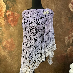 May include: A lavender crochet shawl with a delicate pattern and a white butterfly brooch. The shawl is displayed on a black mannequin.