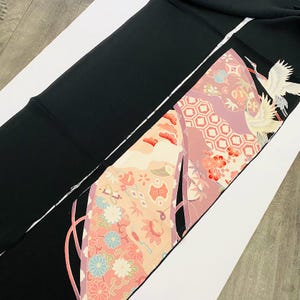 Könnte beinhalten: Schwarzer Stoff mit einem dekorativen Panel mit einem Kranich-Design. Das Panel hat rosa, pfirsichfarbene und weiße Blumen- und geometrische Muster. Der Kranich ist weiß mit schwarzen Akzenten.