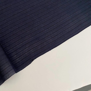 May include: Close-up of navy blue fabric with a ribbed texture. The fabric is angled across a white surface, showing the texture and colour variations. The fabric's edges are visible.