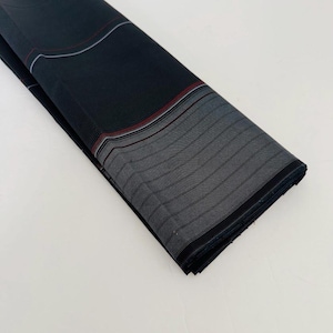 Pode incluir: Uma peça de tecido cinza-escuro dobrada com um padrão de riscas finas repetitivas. O tecido é acentuado com uma borda horizontal distinta composta por linhas paralelas finas em tons de branco, cinza-claro e um vermelho subtil.