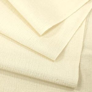 May include: A folded piece of off-white fabric with a visible, fine-grained, horizontal ribbed texture. The material is layered, showing multiple overlapping sections of the light-colored textile with a consistent weave pattern throughout the surface.