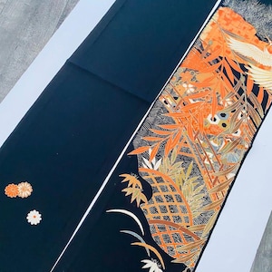 Könnte beinhalten: Schwarzer Stoff mit einem verzierten orangefarbenen und goldenen Blumenmuster an einer Kante. Das Design umfasst stilisierte Blätter, Blumen und einen Vogel. Der Stoff ist wahrscheinlich ein dekorativer Stoff oder ein Kleidungsstück.