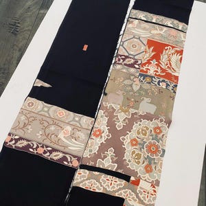Könnte beinhalten: Schwarzer Stoff mit dekorativen Paneelen mit floralen, Vogel- und geometrischen Mustern in Rot-, Grau- und Brauntönen. Der Stoff hat eine rechteckige Form, möglicherweise ein Kimono oder Obi.