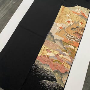 Könnte beinhalten: Ein schwarzer Stoff mit einem dekorativen Panel mit einem Landschaftsdesign. Das Panel zeigt Berge, Bäume und ein Gebäude mit Farben wie Gold, Rosa und Grün. Der Stoff ist wahrscheinlich ein Stück Stoff oder ein Kleidungsstück.