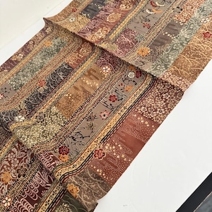 May include: A textile fabric featuring a patchwork design of vertical stripes in shades of brown, tan, and muted green. The pattern includes intricate floral motifs, small blossoms, and geometric textures printed across the surface.