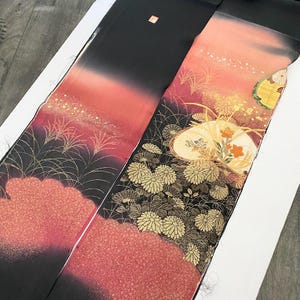 Könnte beinhalten: Zwei dekorative japanische Obi-Gürtel. Einer zeigt einen Schwarz-Rot-Verlauf mit goldenen Akzenten und einem wolkenartigen Muster. Der andere hat einen schwarzen Hintergrund mit goldenen Blumen- und Fächerdesigns und einem roten wolkenartigen Muster.