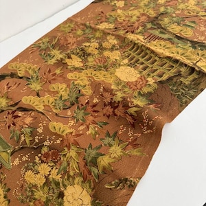 May include: A rectangular fabric runner featuring a rich copper-brown background with an intricate woven pattern of yellow chrysanthemums, green pine branches, and red and green maple leaves, accented by a structured lattice fence design.