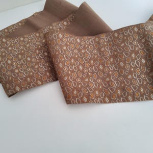 May include: A folded brown fabric with a repeating pattern of small, irregular shapes in gold and white. The fabric has a textured appearance and is likely used for decorative purposes or clothing.