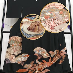Könnte beinhalten: Schwarzer Kimono mit detaillierter Stickerei. Das Design umfasst Fächer, Blumen und einen Vogel. Die Nahaufnahme zeigt komplizierte Muster und Farben, darunter Rot, Braun und Blau. Das Kleidungsstück ist wahrscheinlich aus fließendem Stoff.