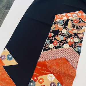 Könnte beinhalten: Ein schwarzer Stoff mit einem dekorativen gemusterten Abschnitt. Der gemusterte Abschnitt zeigt orange, rote und beige Paneele mit Blumen- und Vogelmotiven. Der Stoff hat eine japanische Ästhetik.