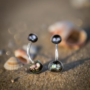 Puede incluir: Un par de anillos de ombligo de plata con cuentas de concha negra e iridiscente.