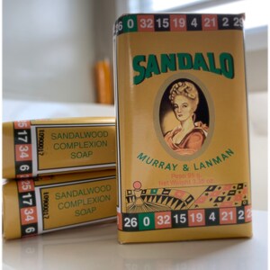 May include: Three rectangular bars of Sandalo Sandalwood Complexion Soap by Murray & Lanman in yellow packaging. The labels feature a portrait of a person, roulette wheel graphics, and the text 'Peso 95 g. Net Weight 3.35 oz.' printed on the front.