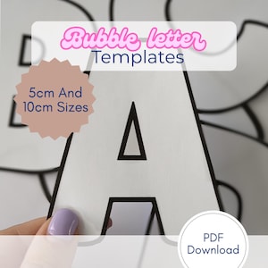 Puede incluir: Plantillas de letras burbuja blancas con contornos negros, con la letra "A". La imagen incluye texto que indica tamaños de 5 cm y 10 cm, y "PDF Download". Las plantillas son sostenidas por una mano con esmalte de uñas morado.