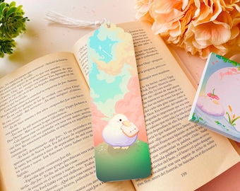 May include: A colorful bookmark featuring a white bird with a pink beak holding a piece of bread. The background is a pastel blue, green, and pink sky with clouds and stars. The bookmark has a tassel.