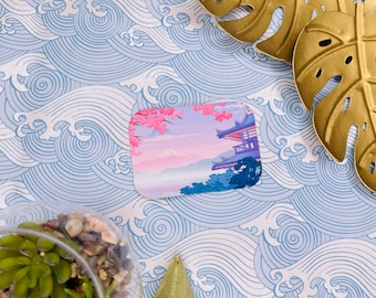 Può includere: Un adesivo rettangolare con un design di ispirazione giapponese. L'adesivo presenta una montagna rosa e bianca, un pagoda blu e fiori di ciliegio rosa. Lo sfondo è blu chiaro con un motivo a onde bianche.