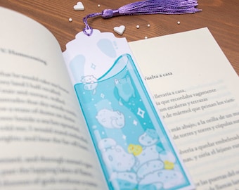 May include: A blue and white bookmark with a purple tassel. The bookmark features a cartoon illustration of a cat in a glass of water with other cats and fish swimming around it. The bookmark has a scalloped edge and a white background.