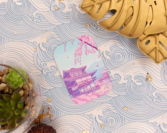 Può includere: Un'illustrazione rosa e blu di un tempio giapponese con fiori di ciliegio. L'illustrazione è stampata su una carta bianca con angoli arrotondati.