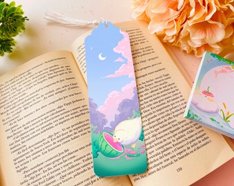 May include: A whimsical bookmark featuring a duck enjoying watermelon under a pastel sky with a crescent moon. The bookmark has a tassel and is set against an open book. The overall theme is reading and summer.