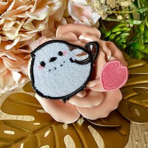 Puede incluir: Un parche bordado de un pájaro blanco y marrón con un parche en forma de corazón rosa. Los parches están en una flor rosa.