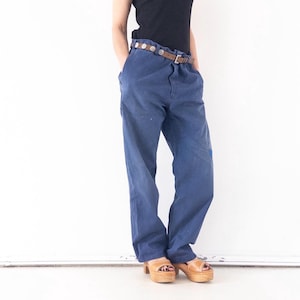 Könnte beinhalten: Eine Person trägt ein schwarzes Tanktop, einen braunen Gürtel mit silbernen Akzenten, eine blaue Jeanshose und braune Plateau-Sandalen.