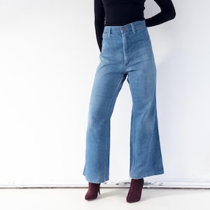Op de afbeelding: Lichtblauwe jeans met hoge taille en wijde pijpen, gecombineerd met een zwarte coltrui met lange mouwen. De jeans heeft een klassiek ontwerp met vijf zakken en een knoopsluiting. De outfit wordt gecompleteerd met bordeauxkleurige enkellaarsjes.