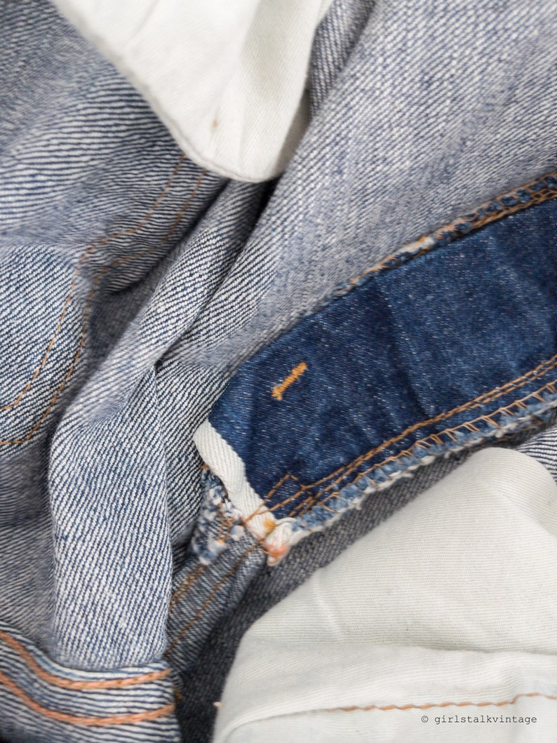 Peut inclure: Gros plan sur un tissu en jean bleu avec un panneau bleu fonc&eacute; contrastant et une doublure en tissu blanc. Le denim a un motif de tissage diagonal subtil.