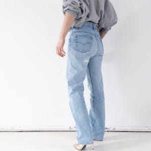 Può includere: Jeans di denim azzurro chiaro con un lavaggio sbiadito e un classico design a cinque tasche. I jeans sono abbinati a una felpa grigia e tacchi dorati. I jeans hanno una vestibilità a gamba dritta.