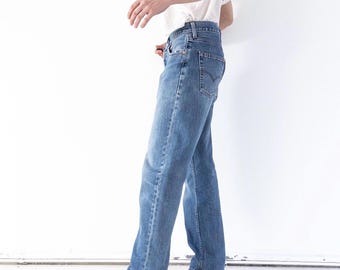 May include: Blue denim jeans featuring a classic five-pocket design, a mid-rise waist, and a straight-leg cut. The jeans have visible copper-toned rivets, a button fly closure, and a stitched arcuate pattern on the back pockets.