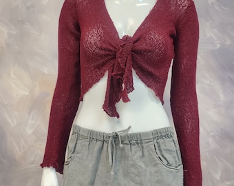 May include: A maroon knit crop top with a tie front and long sleeves. The top has a loose, flowy fit and a slightly ruffled hem.