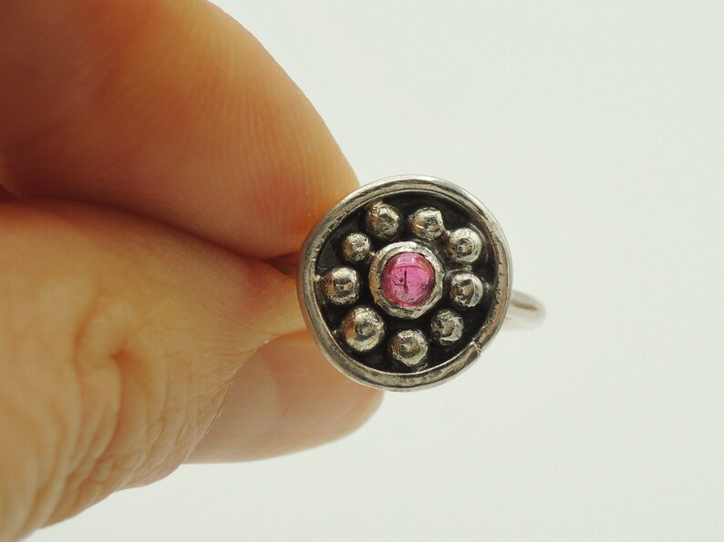 May include: A silver ring with a pink gemstone surrounded by small silver beads.