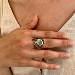 May include: A silver ring with a geometric design featuring a green gemstone. The ring is set in a modern, abstract style.