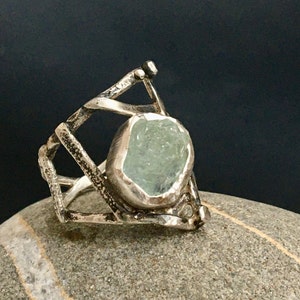 May include: A silver ring with a geometric design and a light blue aquamarine gemstone.