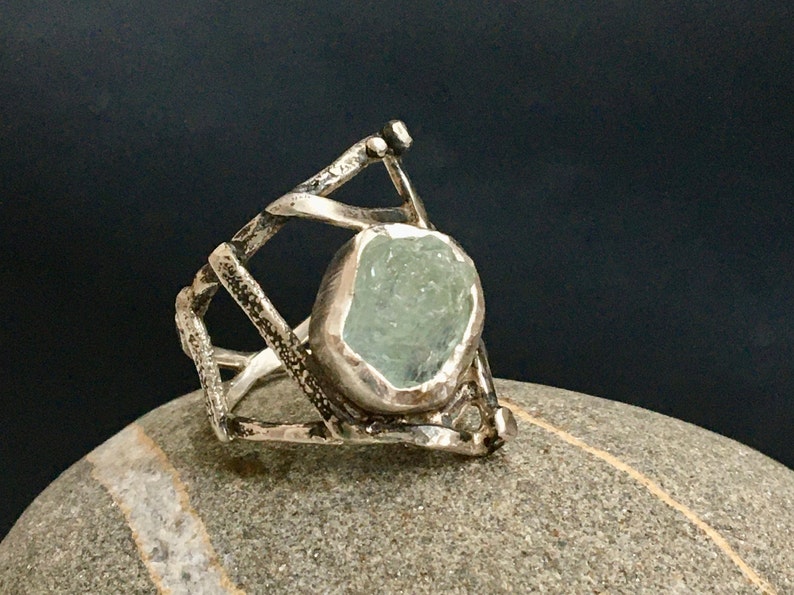 May include: A silver ring with a geometric design and a light blue aquamarine gemstone.