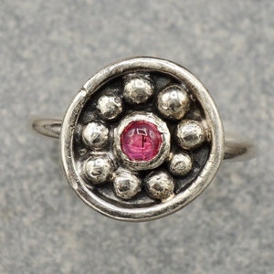 May include: A silver nose ring with a pink gemstone surrounded by small silver beads.