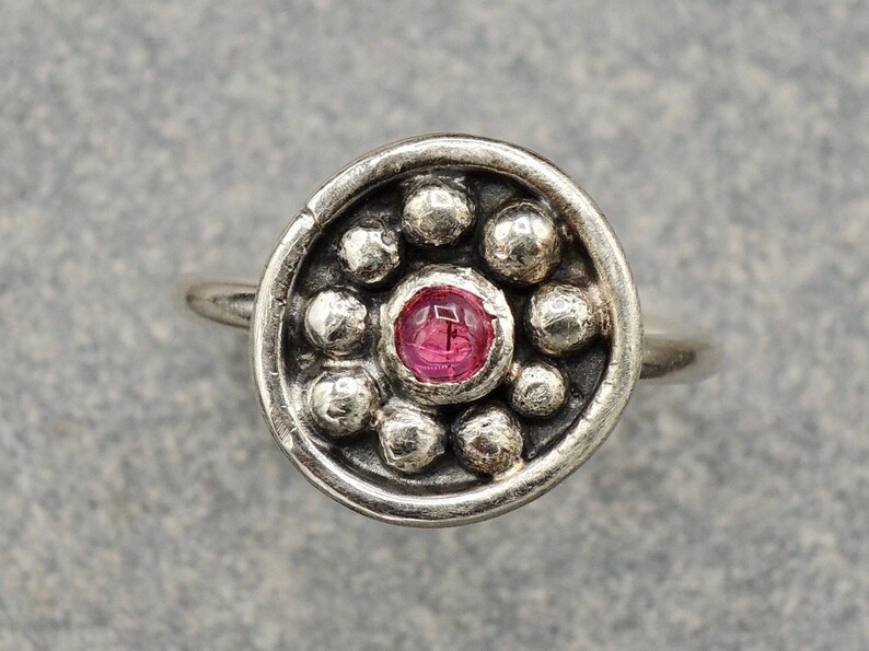 May include: A silver nose ring with a pink gemstone surrounded by small silver beads.