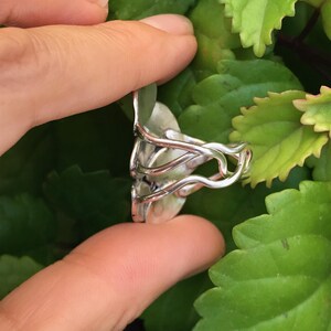 May include: A silver ring with a unique design featuring multiple intertwined bands and a round, slightly raised, silver centerpiece.
